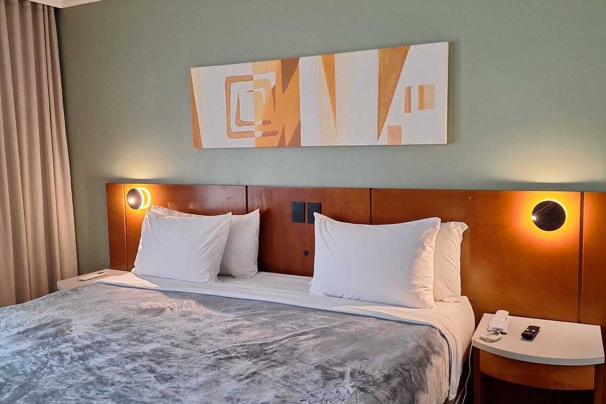 A hotel room with a bed, a headboard, a wall-mounted artwork, a bedside table with a phone, and a nightstand.