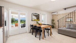 A spacious living area with a dining table, black chairs, a grey sofa, and a staircase with stone walls.