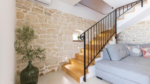 A staircase with wooden steps and black metal railings, leading to a room with a grey sofa and a decorative vase with green plants.