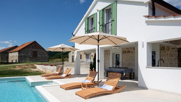 A poolside area with lounge chairs and umbrellas, a stone building in the background, and a clear blue sky.