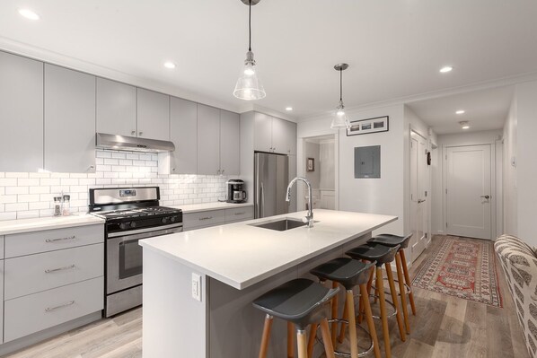 A modern kitchen with grey cabinets, a white countertop, a stainless steel stove, and a large island with bar stools.