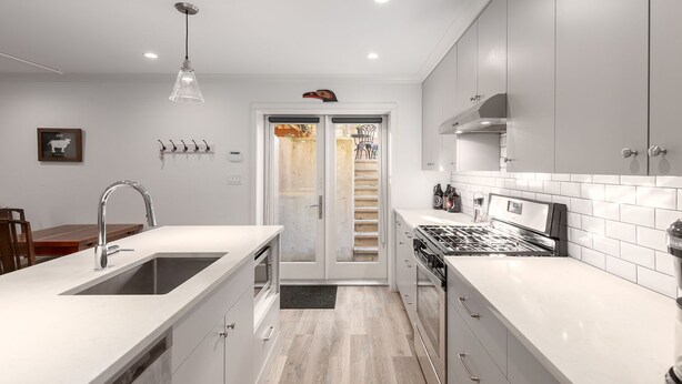Une cuisine moderne avec des meubles blancs, un évier en acier inoxydable et une cuisinière encastrée.