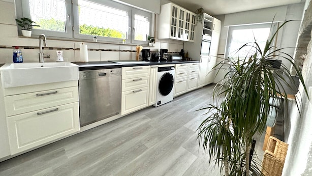 A modern kitchen with white cabinetry, a dishwasher, a washing machine, and a large window providing natural light. - Refugium 2020 - The vacation apartment - 69 sqm with balcony, perfect for 4 people, max. 7 (Marienheide)