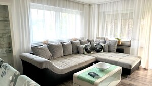 A modern living room with a sectional sofa, a glass coffee table, and a bookshelf. - Refugium 2020 - The vacation apartment - 69 sqm with balcony, perfect for 4 people, max. 7 (Marienheide)