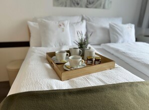 A neatly made bed with a tray of tea cups and jars, a white pillow with a floral design, and a small plant on the bedside table. - Refugium 2020 - The guest apartment - 45 square meters with terrace, perfect for 2 people, max. 4 (Marienheide)
