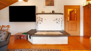 Un soggiorno con camino, soffitto in legno, una TV a schermo piatto montata al muro e una porta che dà su un'altra stanza.