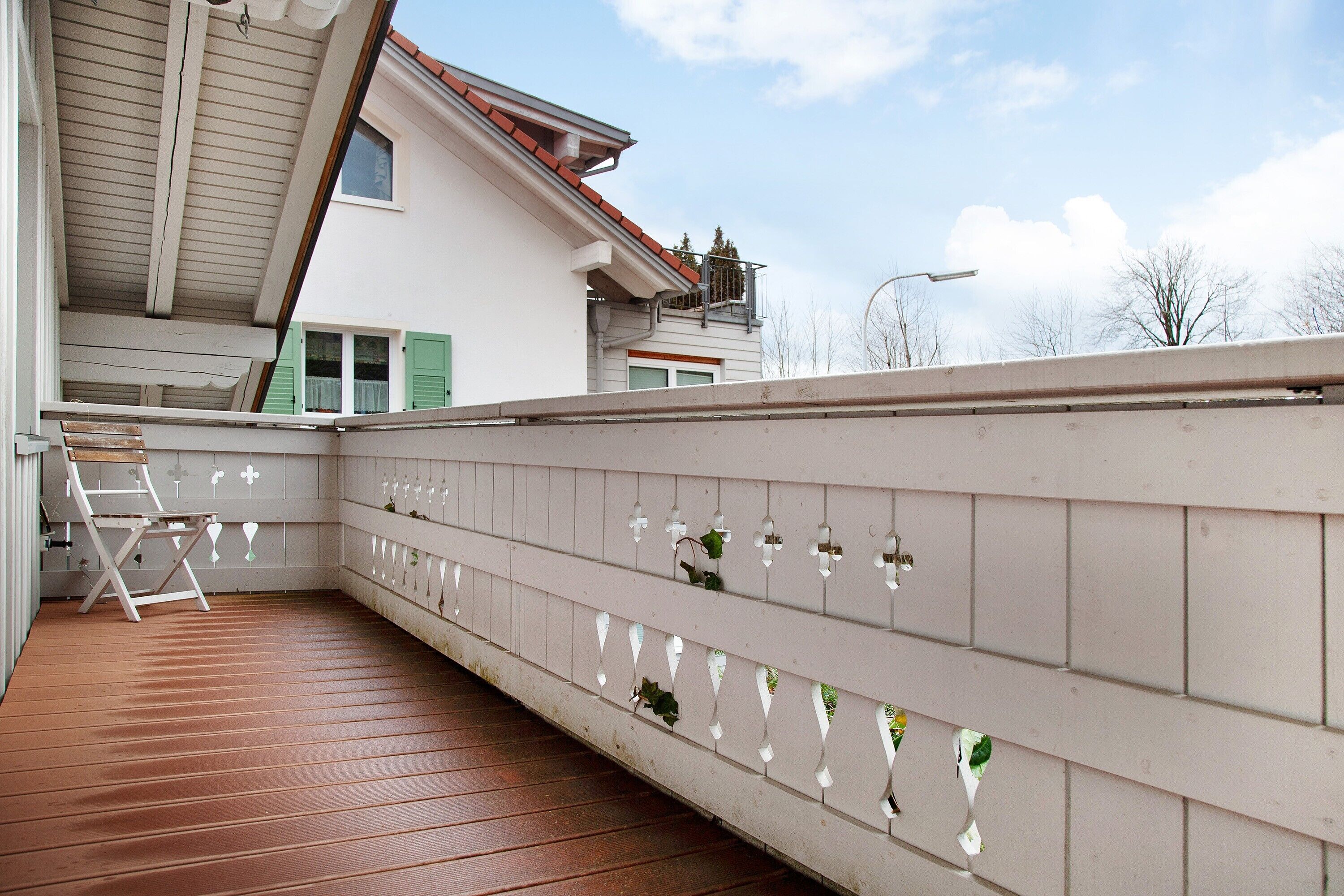 A covered outdoor area with a wooden floor, a white railing with decorative elements, and a ladder.