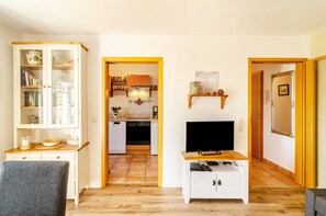 Un espace de vie compact comprenant un coin cuisine, un téléviseur et une bibliothèque.