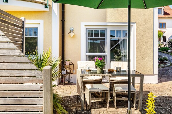 Une terrasse avec des meubles en osier, une table et des chaises, un banc en bois et un parasol vert.