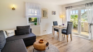 A modern living room with a sofa, a dining table, and a wicker coffee table. - Apartment 'Lavendel' with Private Terrace and Wi-Fi (Hofgeismar)