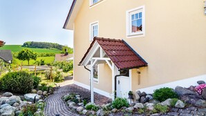 A house with a red roof, a garden with rocks and plants, and a view of green fields. - Apartment 'Lavendel' with Private Terrace and Wi-Fi (Hofgeismar)