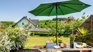 A patio with a table set for dining, a green umbrella, and a view of houses in the background. - Apartment 'Lavendel' with Private Terrace and Wi-Fi (Hofgeismar)