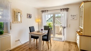A room with a dining table, chairs, a lamp, a mirror, a window with curtains, a door leading outside, and a wall with a framed picture and a sign. - Apartment 'Lavendel' with Private Terrace and Wi-Fi (Hofgeismar)