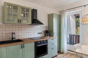 A kitchen with a sink, stove, and cabinets, a window with a view, and a door leading to an outdoor area. - Apartment 'Hubert' with Mountain View, Balcony and Wi-Fi (Garmisch-Partenkirchen)