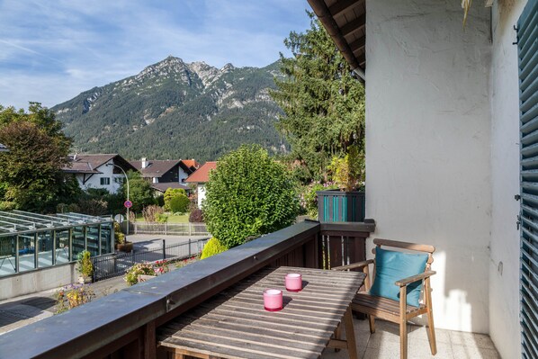 A balcony with a wooden table and two pink candles, overlooking a mountain and houses. - Apartment 'Hubert' with Mountain View, Balcony and Wi-Fi (Garmisch-Partenkirchen)