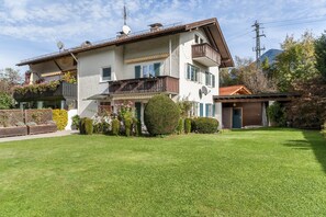 A two-story house with a balcony, a small garden, and a mountain in the background. - Apartment 'Hubert' with Mountain View, Balcony and Wi-Fi (Garmisch-Partenkirchen)