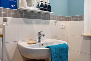 Un baño con un lavamanos blanco, una toalla azul y artículos de aseo en un estante.