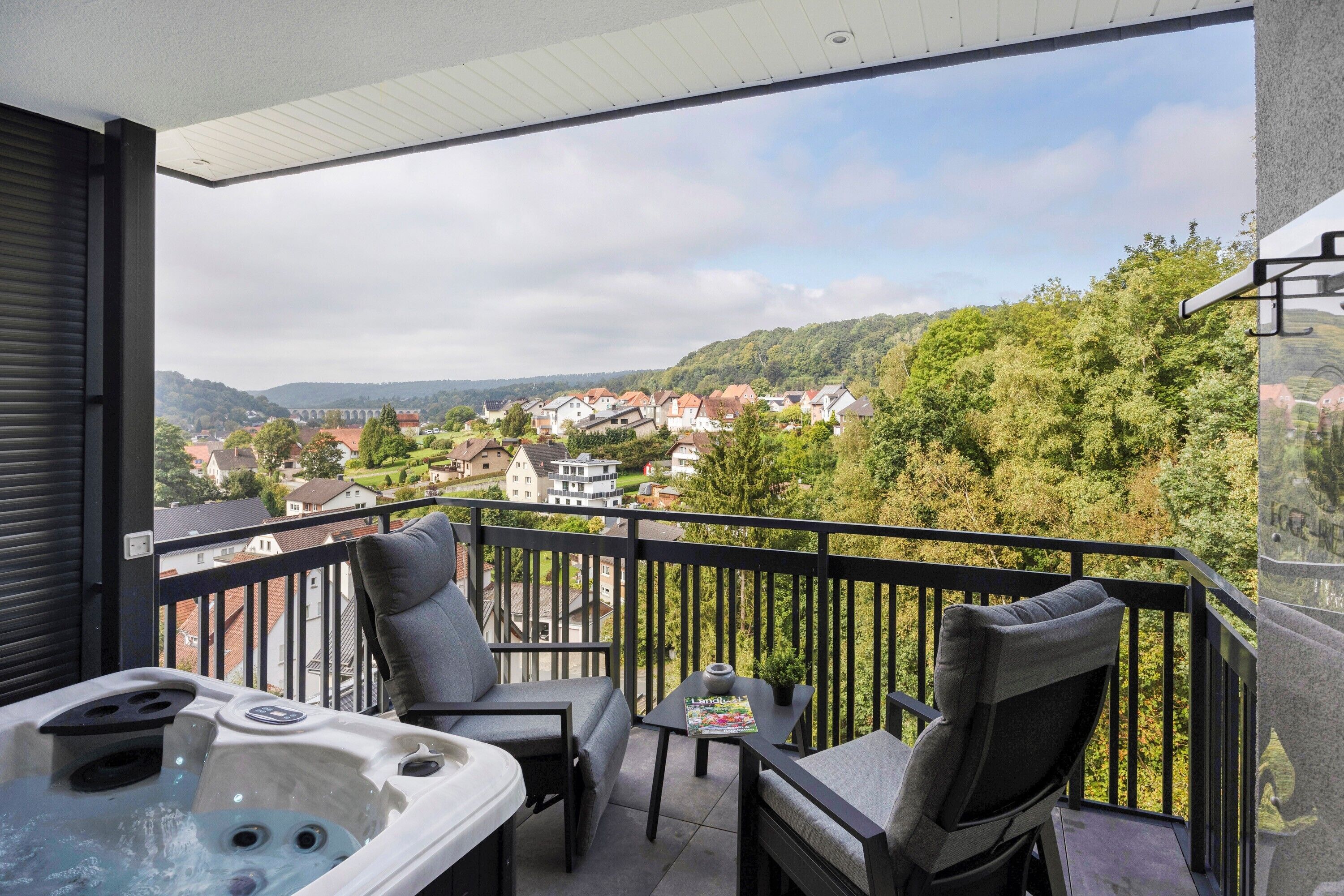 Ein Balkon mit Whirlpool, Sitzgelegenheit und Tisch, mit Blick auf ein Wohngebiet und Hügel.