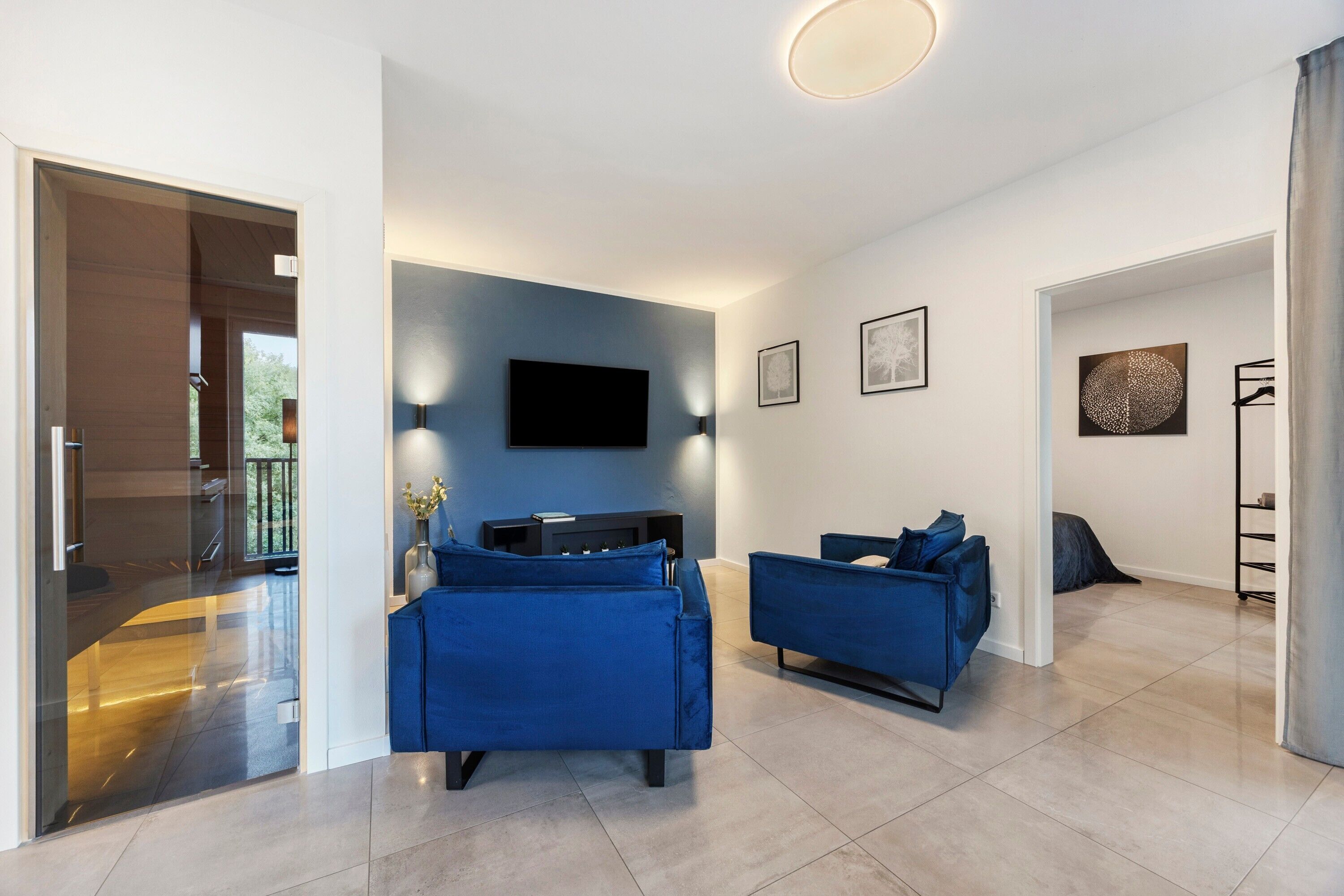 Ein modernes Wohnzimmer mit Flachbildfernseher, blauen Sofas und minimalistischer Einrichtung.