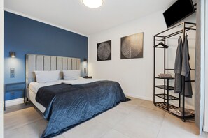 A bedroom with a bed, a bedside table, a wall-mounted TV, and a clothing rack. - Apartment "Egge Resort 7e" with Balcony, Whirlpool & Sauna (Altenbeken)