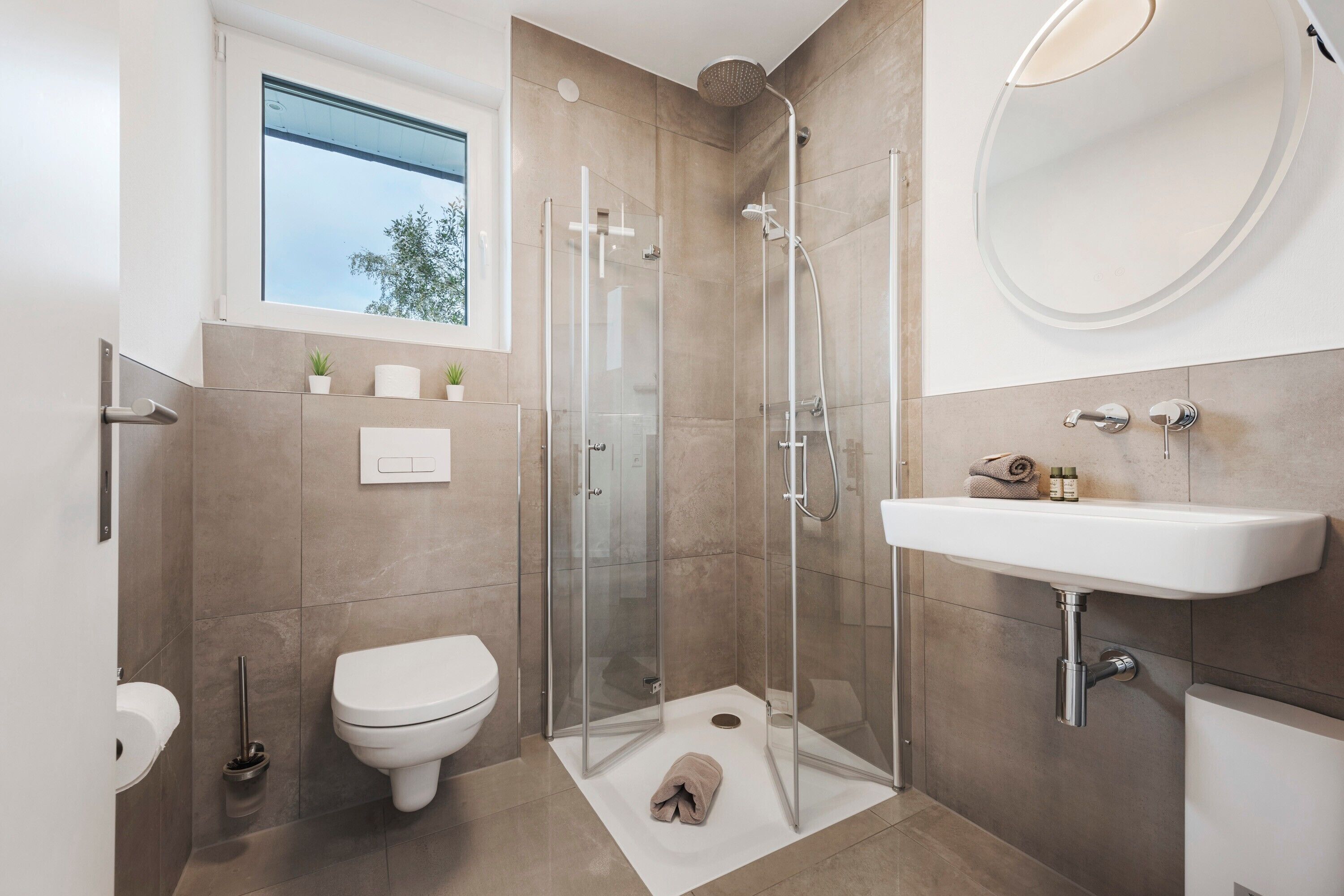 A modern bathroom with a glass shower enclosure, a white sink, and a window above the toilet.