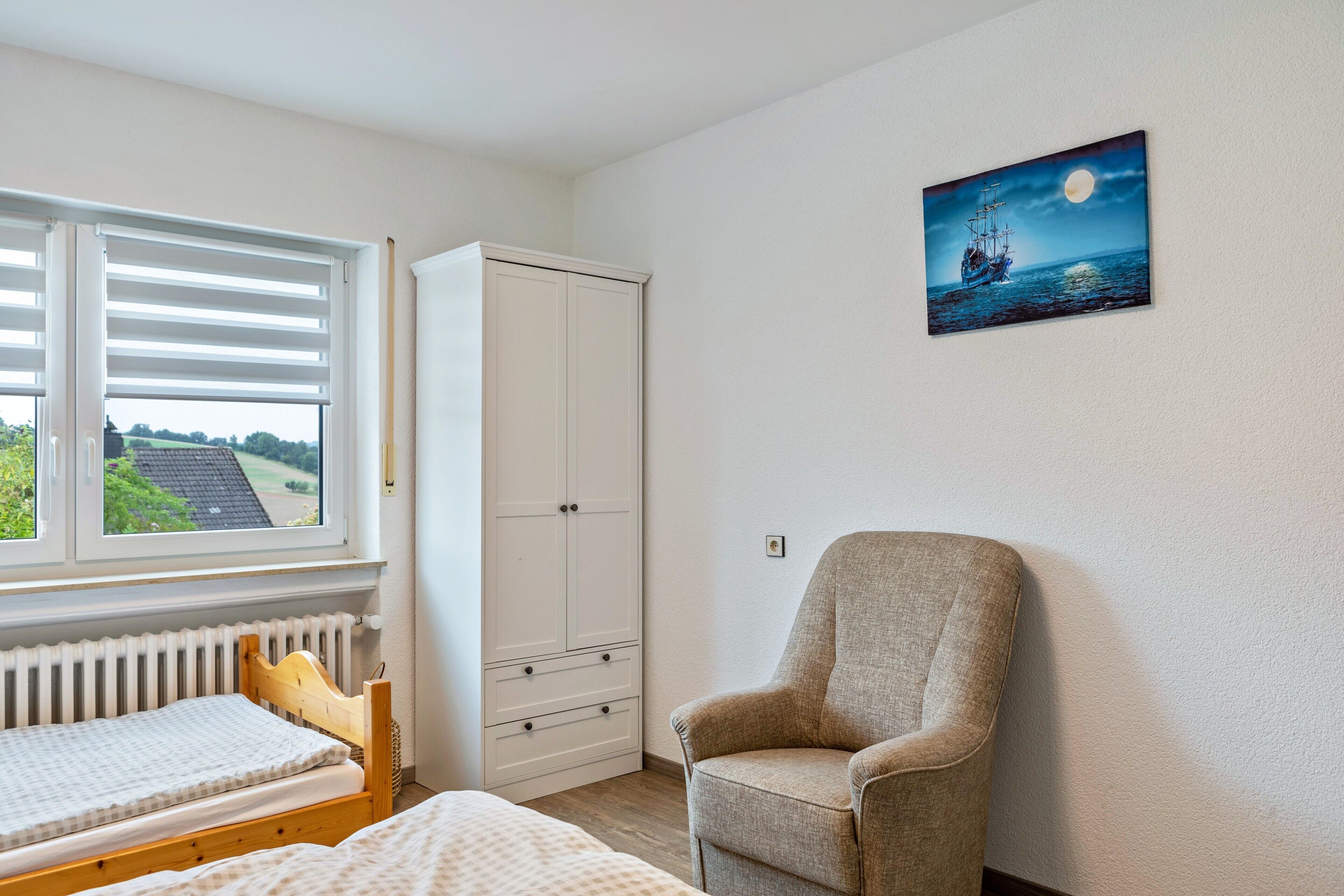 A bedroom with a bed, a chair, a wardrobe, a radiator, and a window with blinds.
