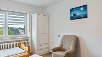 A bedroom with a bed, a chair, a wardrobe, a radiator, and a window with blinds.