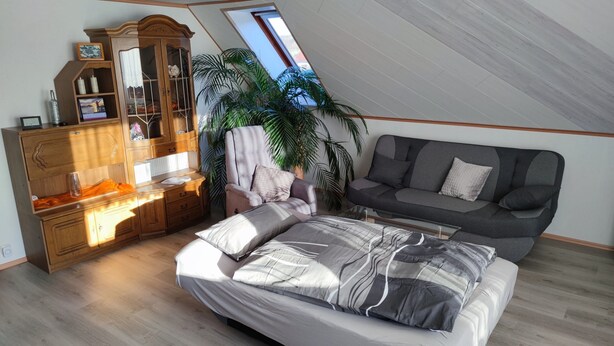 A bedroom with a sloped ceiling, a bed, a sofa, a wooden dresser, and a large window. - Apartment 'Mone's Kloetze' with Private Terrace, Wi-Fi and Air Conditioning (Klötze)
