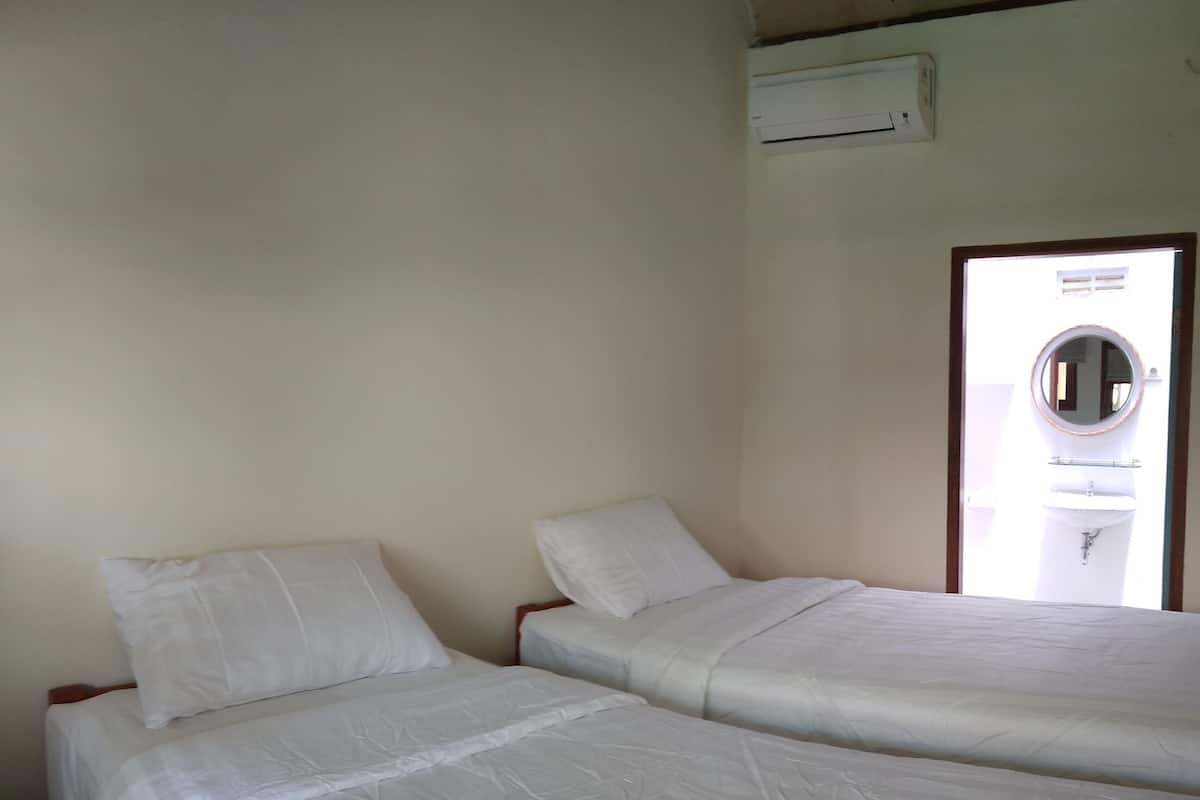 A room with two single beds, a white wall, and a window with a view of the outside.