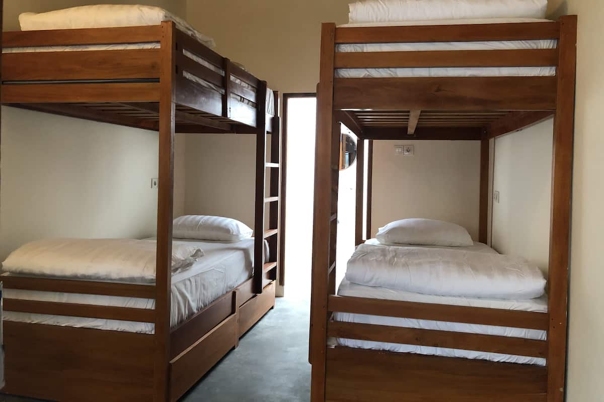 Two bunk beds with wooden frames and white bedding, a ladder, and a door leading to another room.