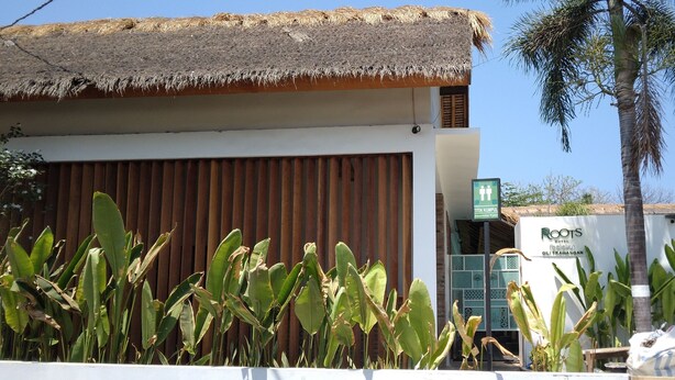 A building with a thatched roof, a sign indicating a hotel, and a flag. - Roots Hotel Trawangan (Gili Trawangan)