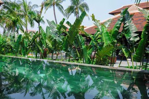 A pool surrounded by lush tropical plants and palm trees, reflecting the greenery. - Su Retreat Hoi An - Riverfront Resort (Da Nang)