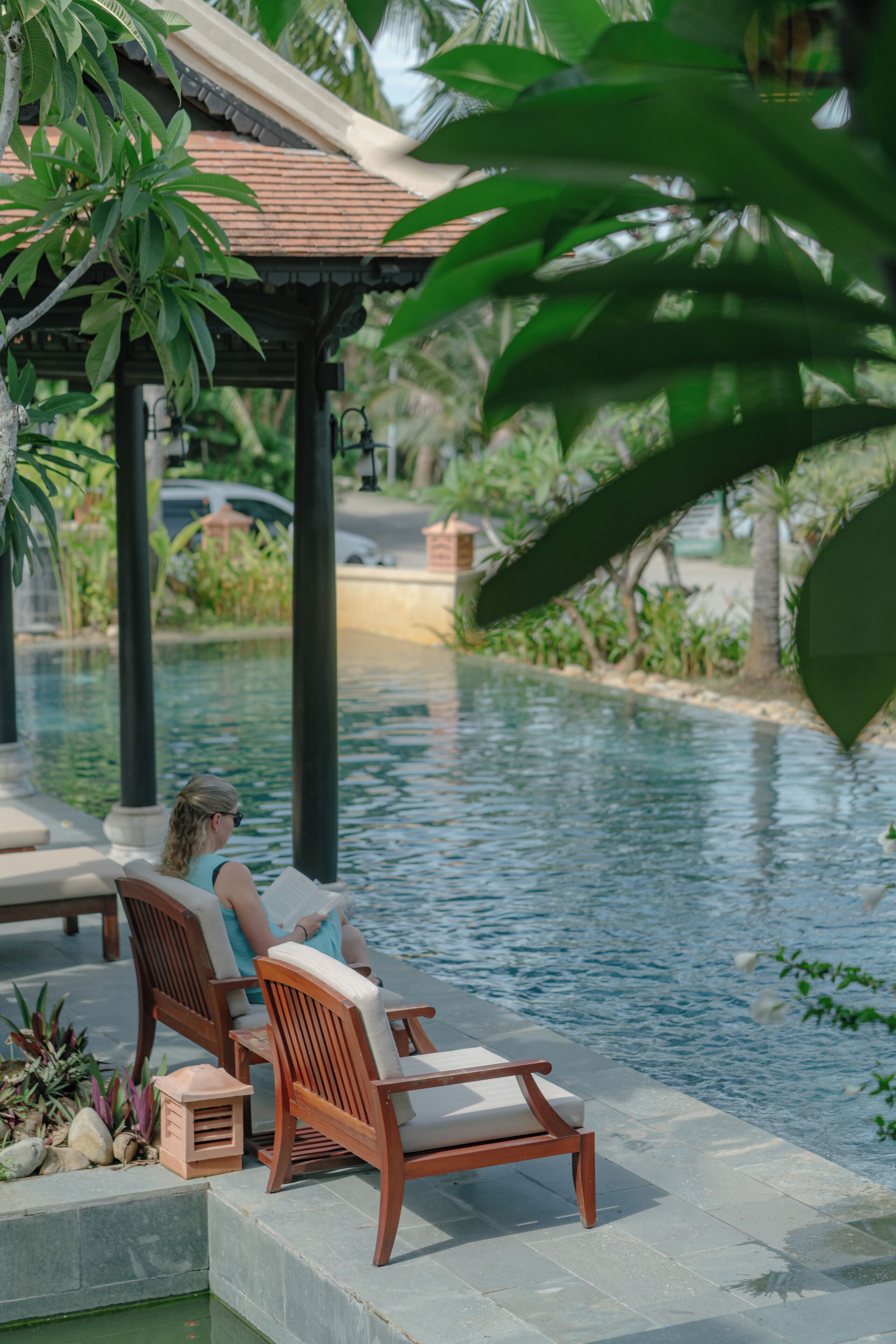 A poolside area with wooden chairs and a person reading.