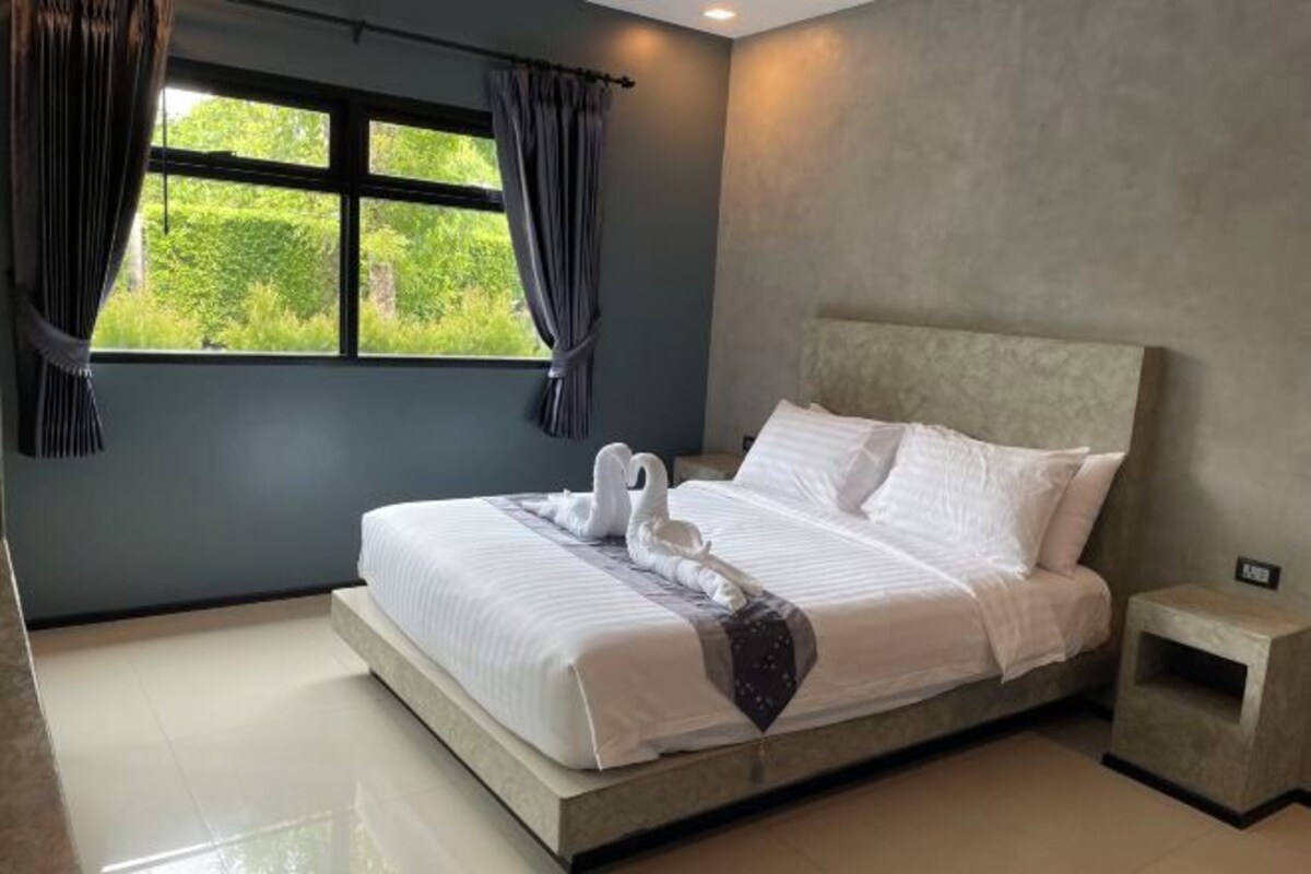 A modern bedroom with a large bed, grey walls, and a view of greenery outside.