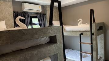 Habitación de hotel con literas, una escalera, una ventana con cortinas, un equipo de aire acondicionado y vistas a zonas verdes.