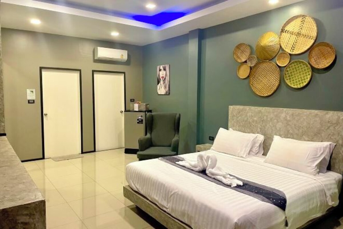 A modern hotel room with a large bed, a green armchair, and a wall decorated with woven baskets.