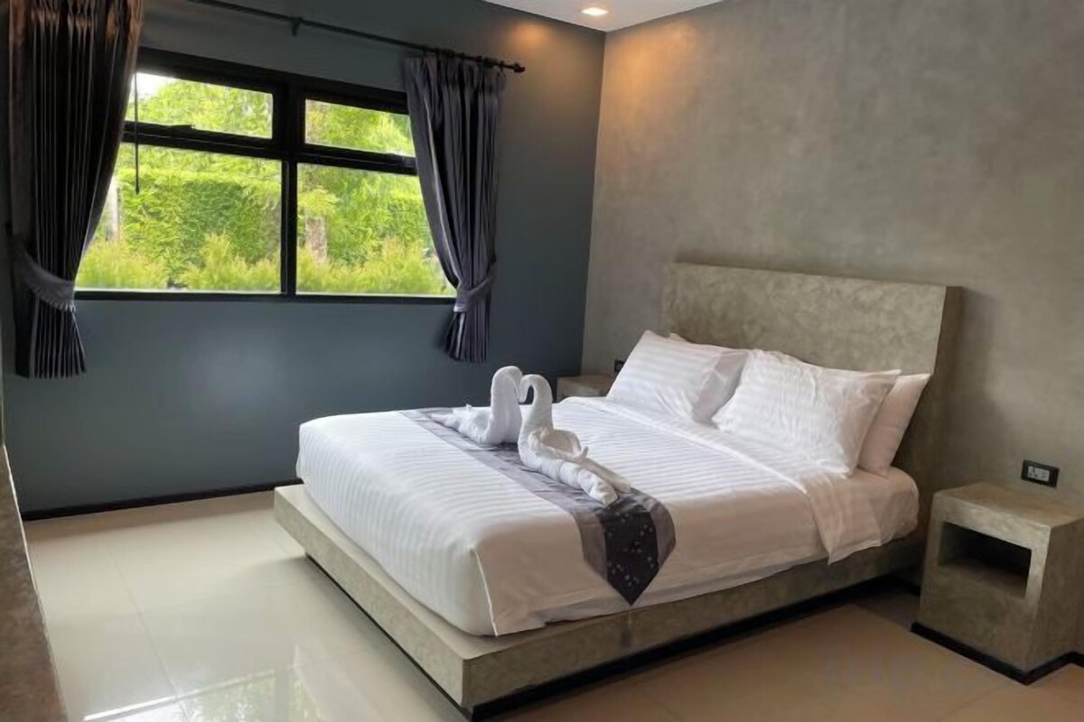 A modern bedroom with a large bed, a nightstand, and a window with curtains.