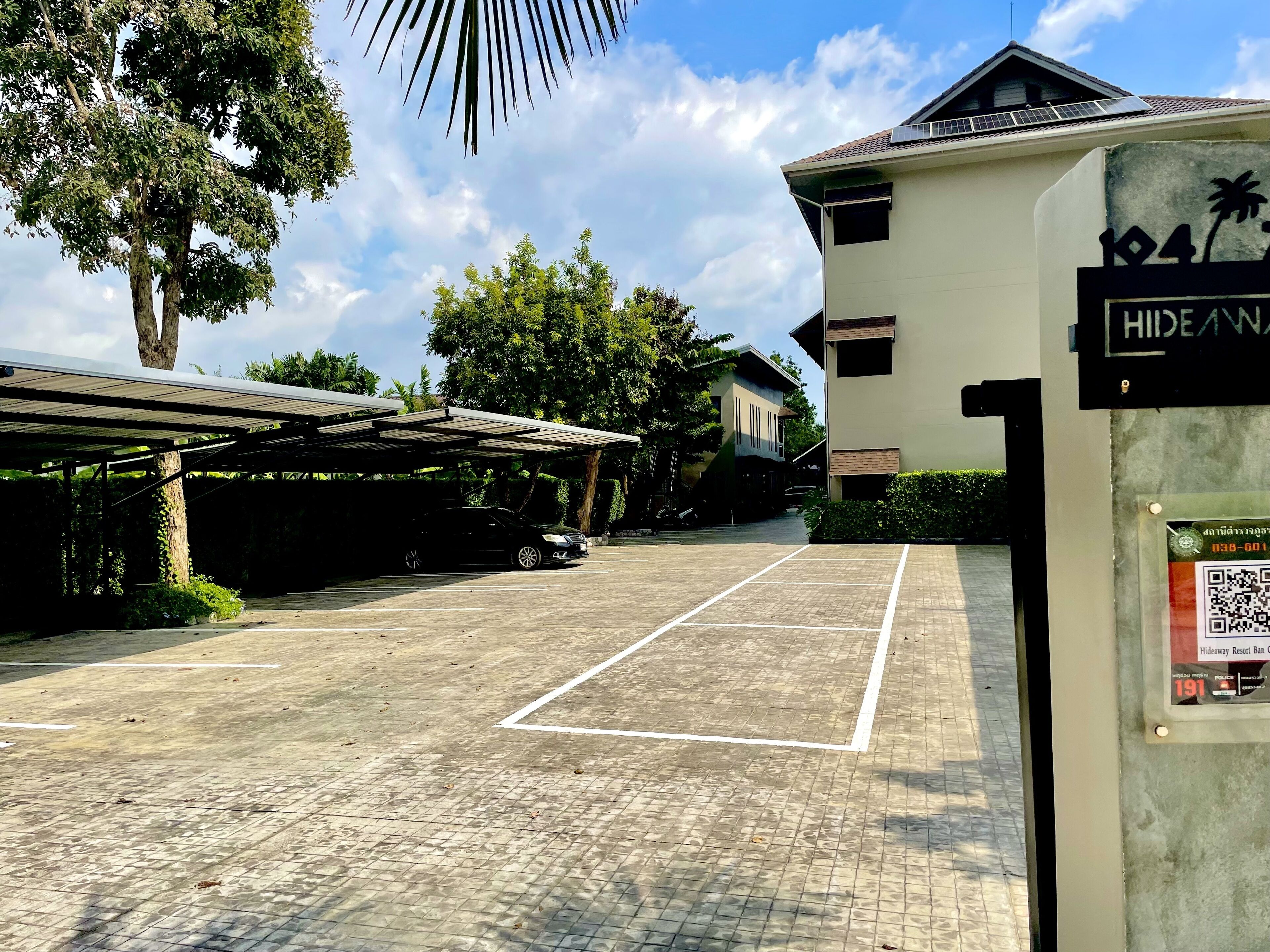 Un área de estacionamiento con superficie pavimentada, una estructura cubierta para coches y un edificio con un letrero que indica 'Hideaway Resort Ban'.