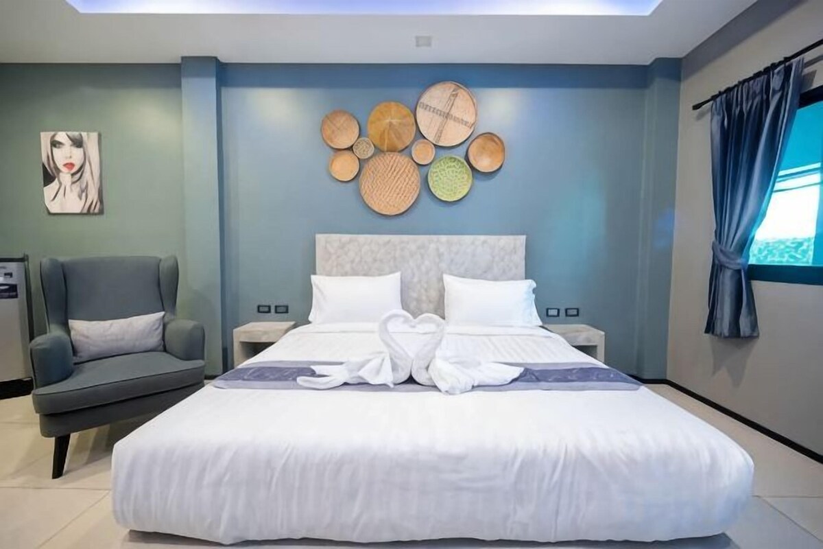 A modern hotel room with a large bed, a bedside table, a chair, and a wall art piece.