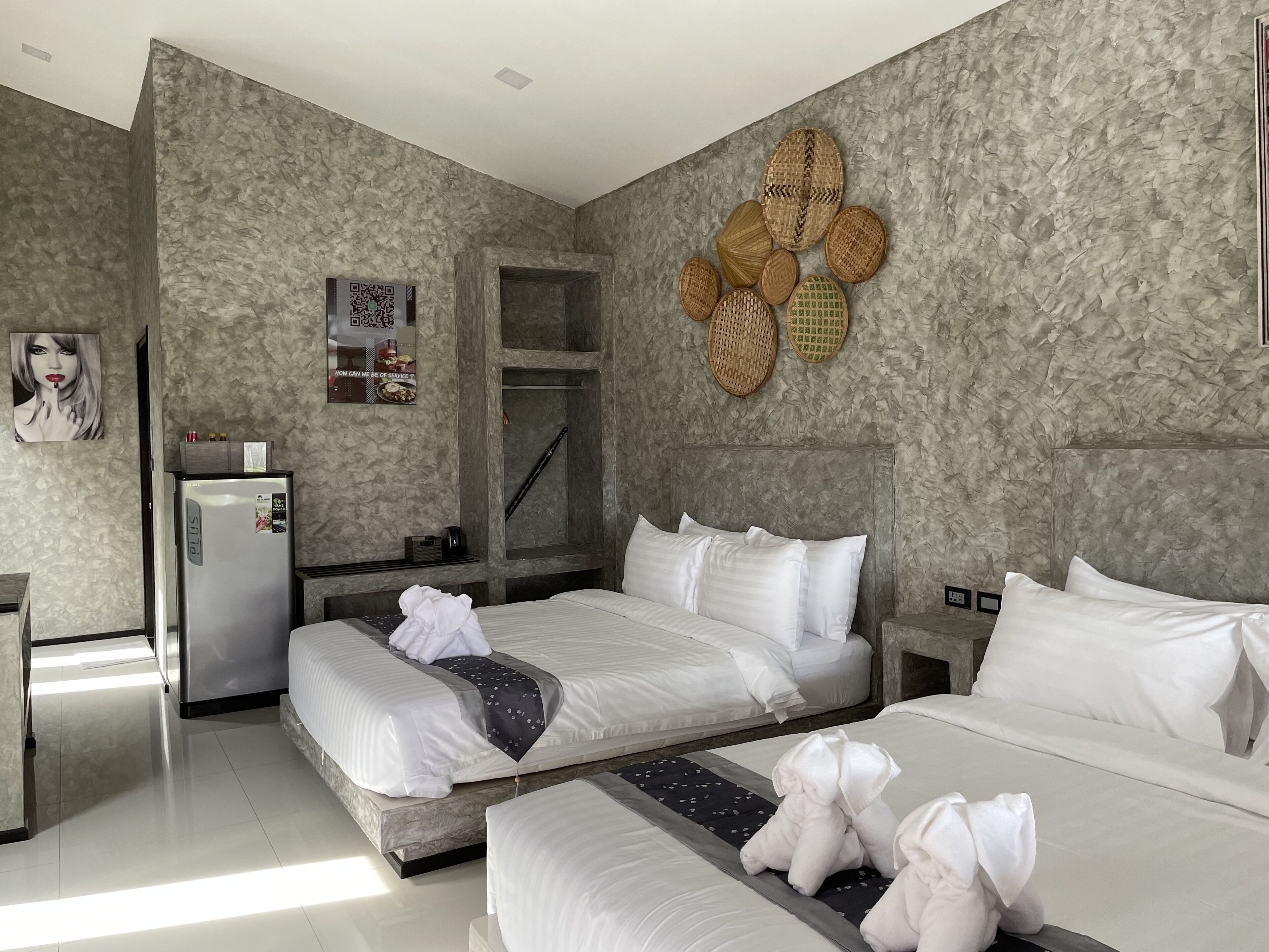 A hotel room with a stone-textured wall, a bed with white linens, a refrigerator, and a small seating area with a table and chairs.