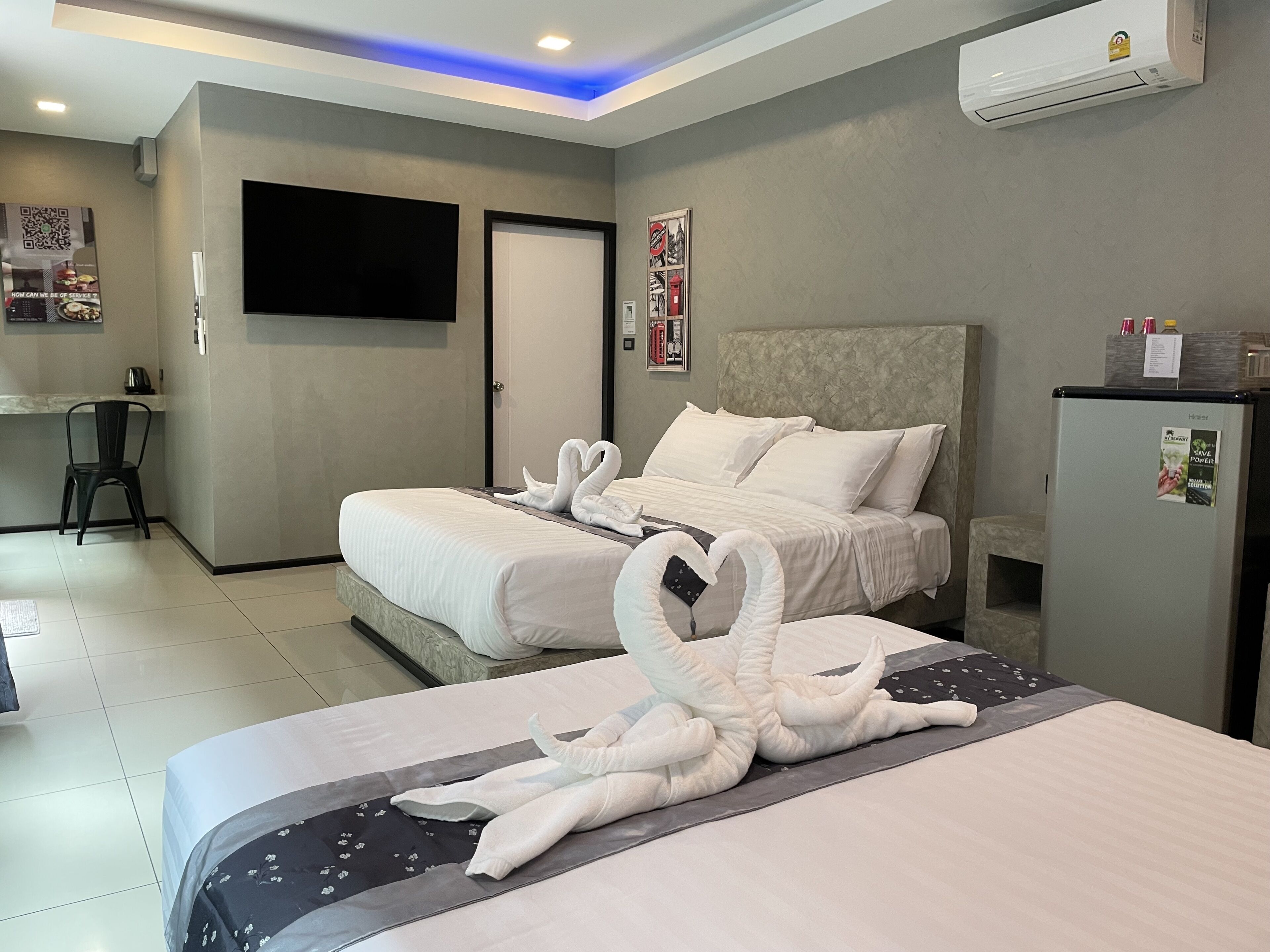 Een hotelkamer met twee bedden, een flatscreen televisie, een koelkast en een bureau met stoel.