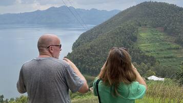 Two people standing on a grassy hill overlooking a lake and mountains.