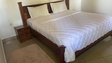 A neatly made bed with a white quilt, a wooden headboard, and a small bedside table with drawers.