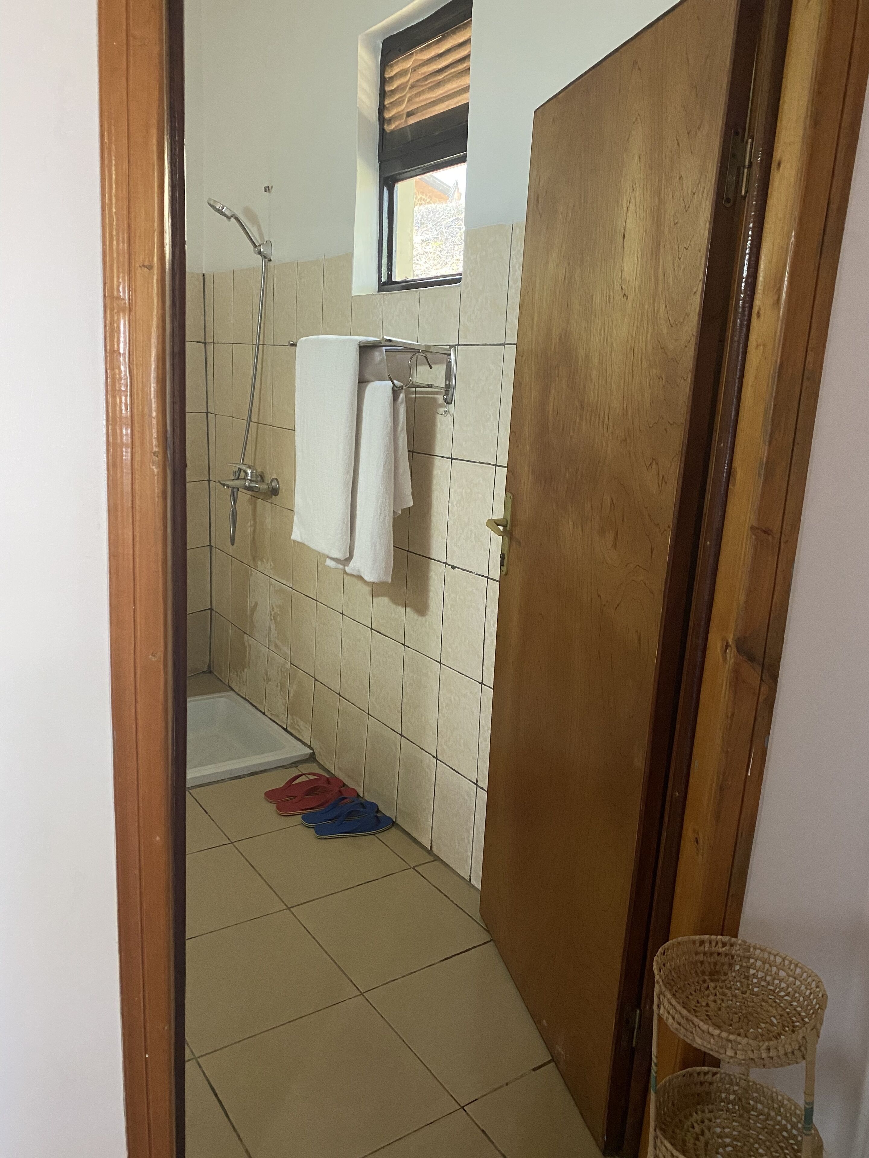 A bathroom with a shower, a towel rack, and a pair of slippers on the floor.