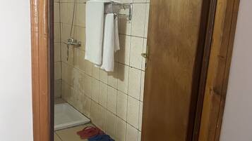 A bathroom with a shower, a towel rack, and a pair of slippers on the floor.
