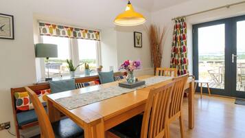 Un comedor con una mesa de madera, sillas, una lámpara colgante amarilla y vistas a través de un ventanal.