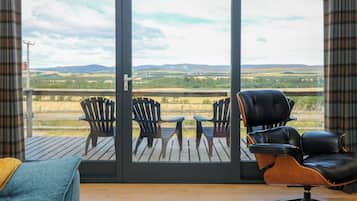 Una habitación con puerta corrediza de vidrio que da a una terraza con sillas y vistas al campo.