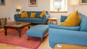 Una sala de estar con un sofá azul, una mesa de centro de madera y una mesita auxiliar.