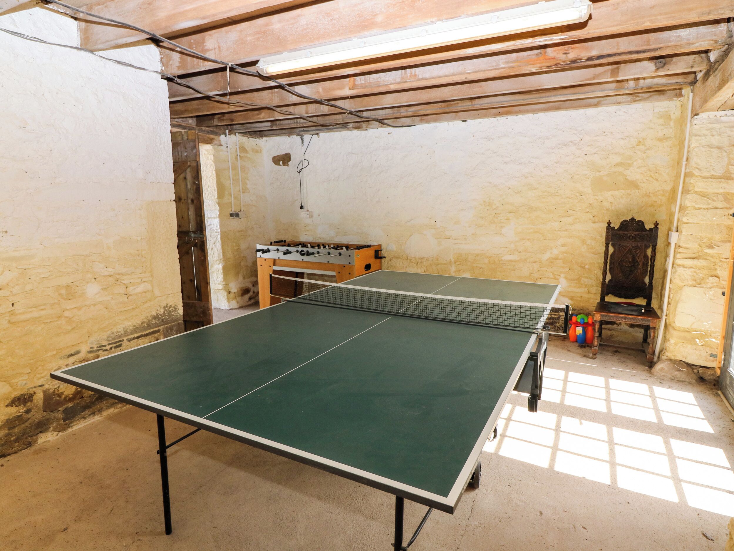 Uma mesa de pingue-pongue em um quarto com paredes de pedra, uma cadeira de madeira e uma mesa de futebol de mesa.