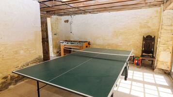 Uma mesa de pingue-pongue em um quarto com paredes de pedra, uma cadeira de madeira e uma mesa de futebol de mesa.